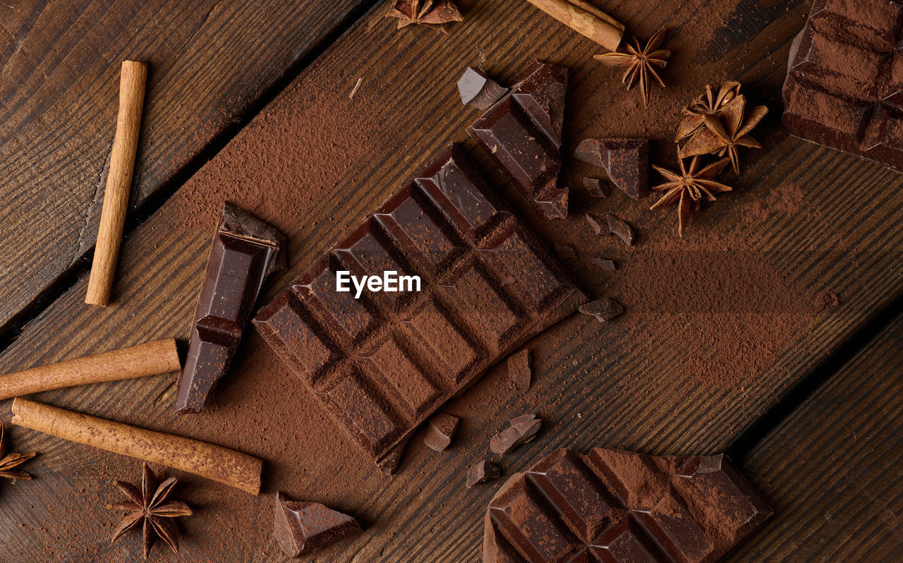Broken pieces of dark chocolate, cinnamon sticks and star anise on a brown wooden table, top view