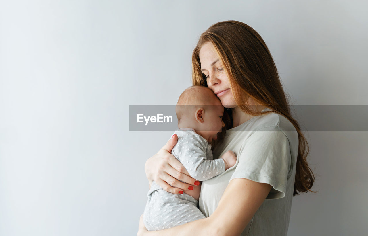 Mother embracing daughter against wall at home