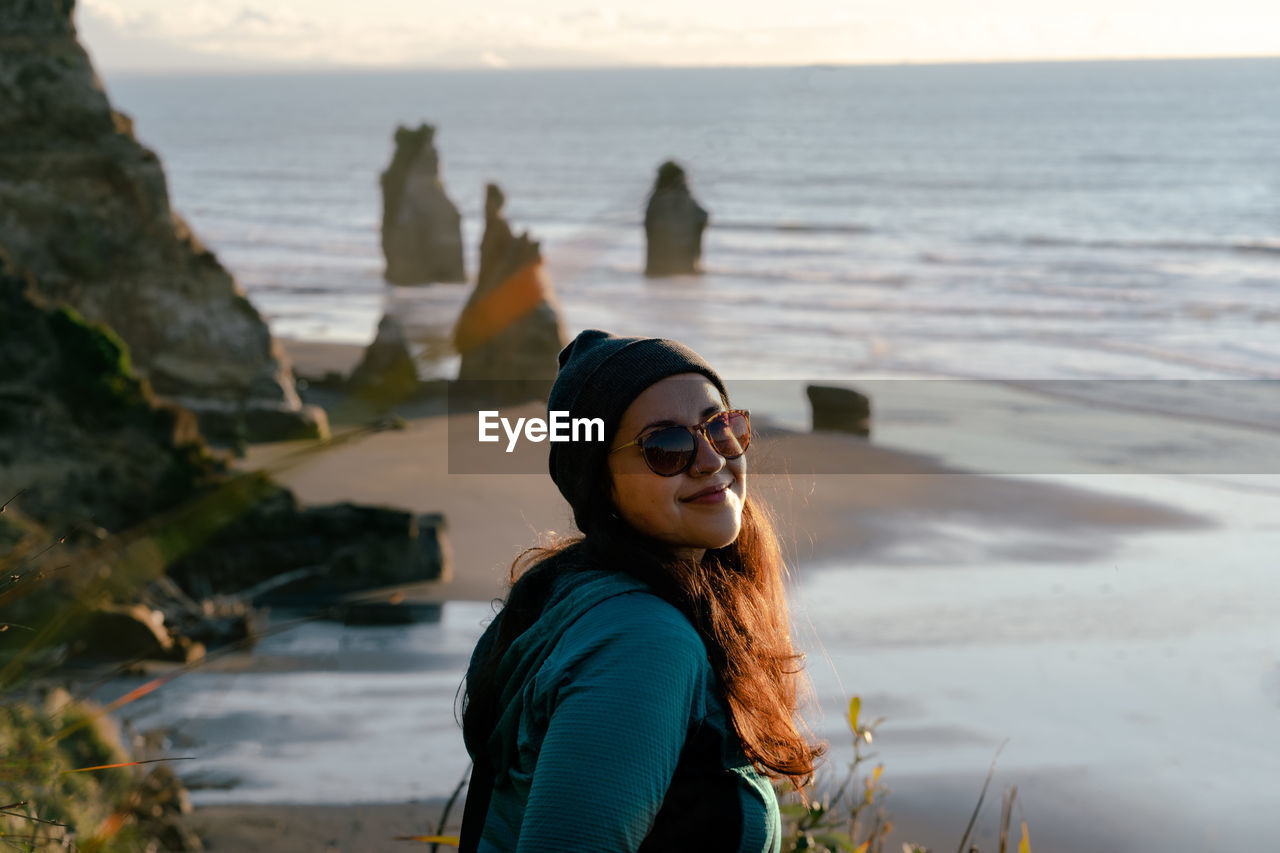 WOMAN WEARING SUNGLASSES ON BEACH AGAINST SKY