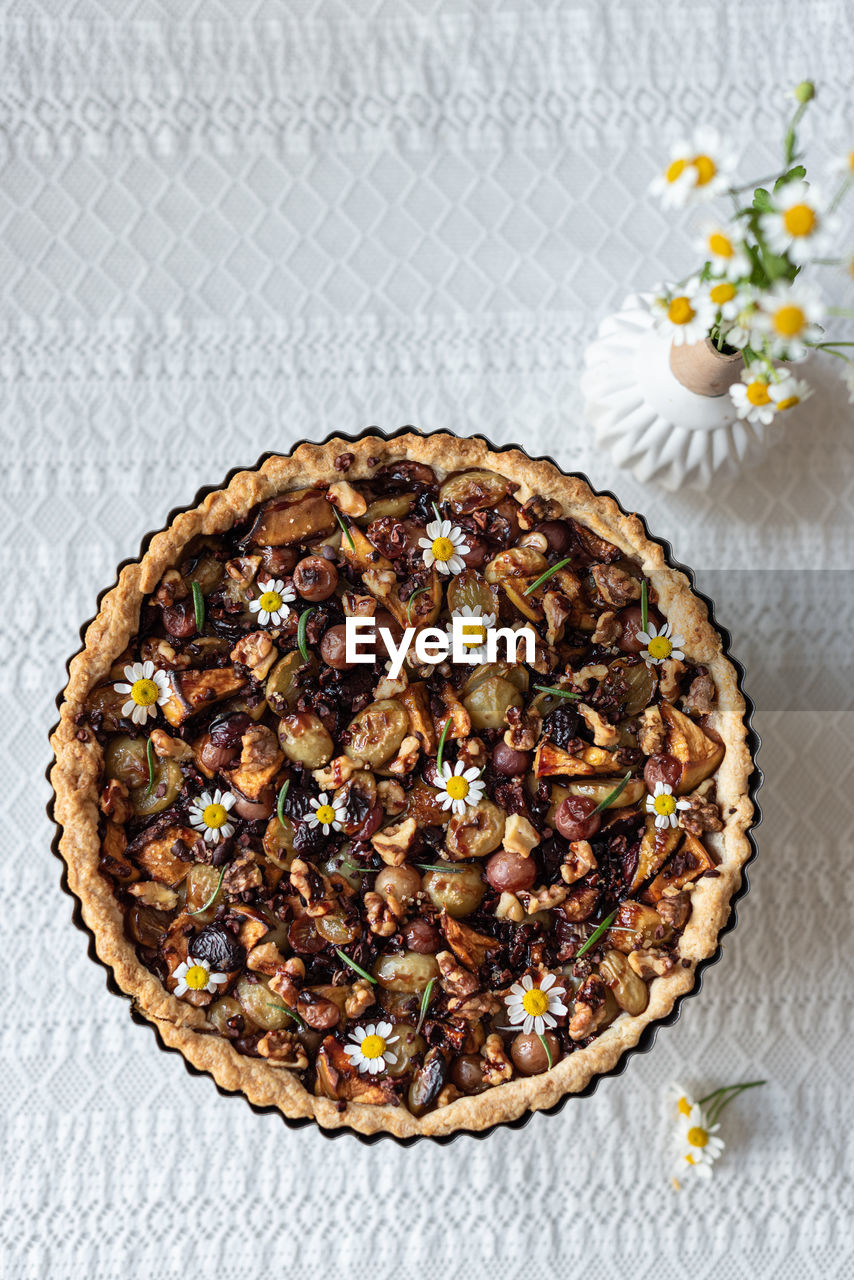Top view of sweet yummy tart with various dried berries served on table with bouquet of chamomile flowers in rustic kitchen