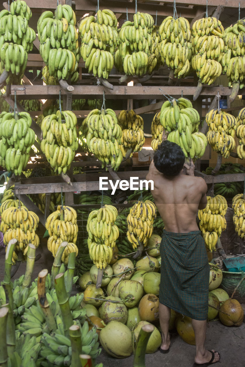 Rear view of shirtless man selling bananas at market