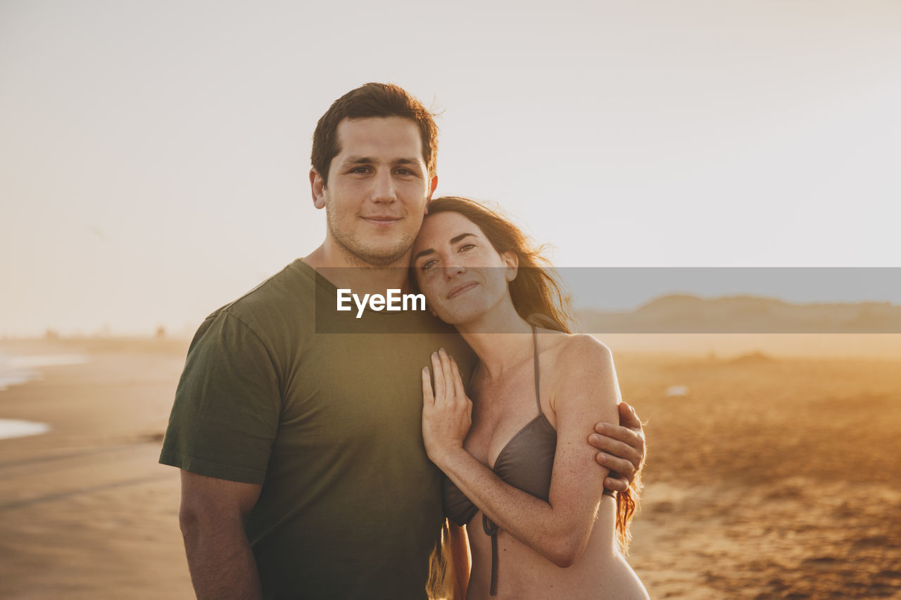 Portrait of young couple standing against sky on beach