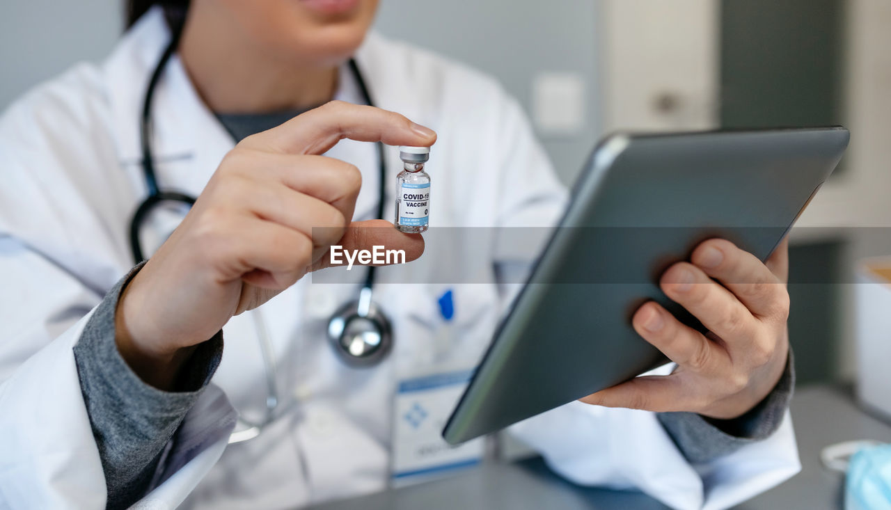 Midsection of doctor holding vaccine using digital tablet