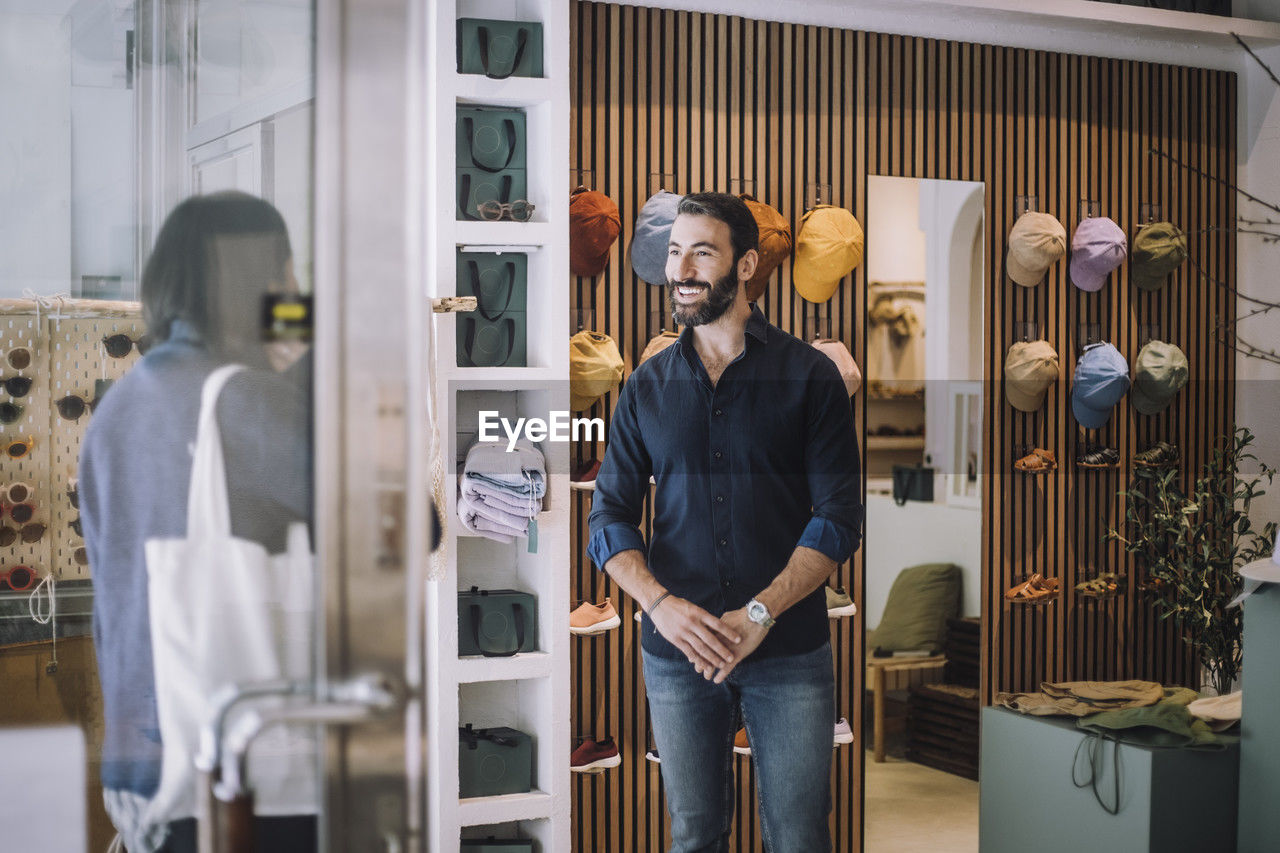 Smiling salesman looking at female customer arriving in clothing store