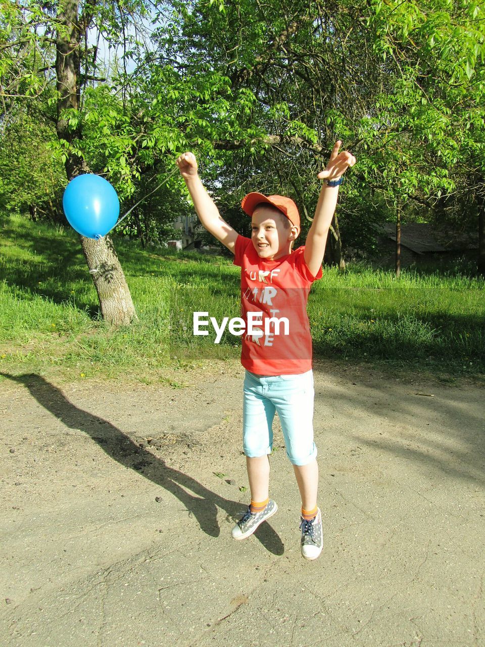 Full length of boy jumping with balloon against tree