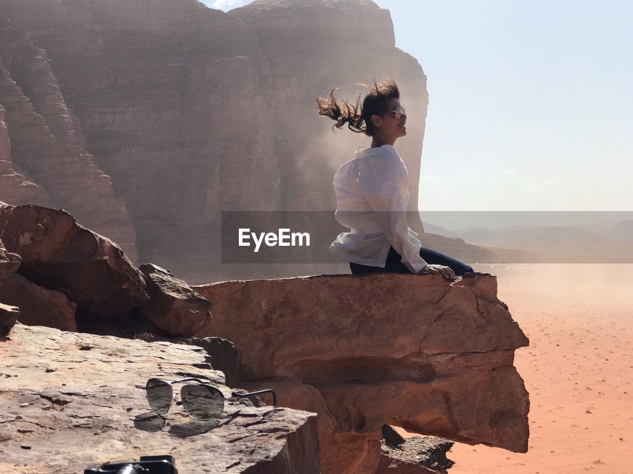 Woman sitting on rock against sky