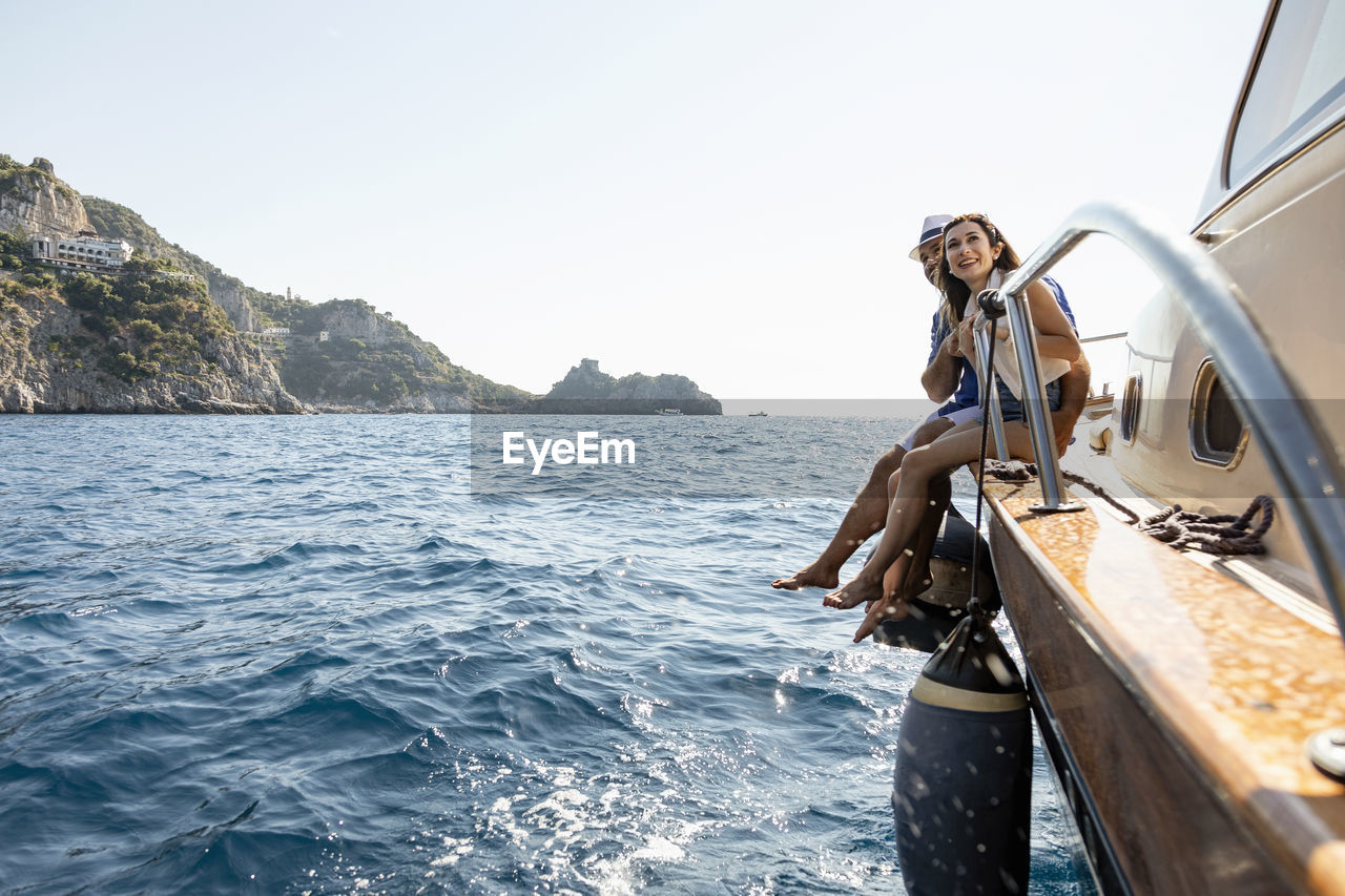 Happy couple sitting at motorboat's edge in amalfi coast, italy