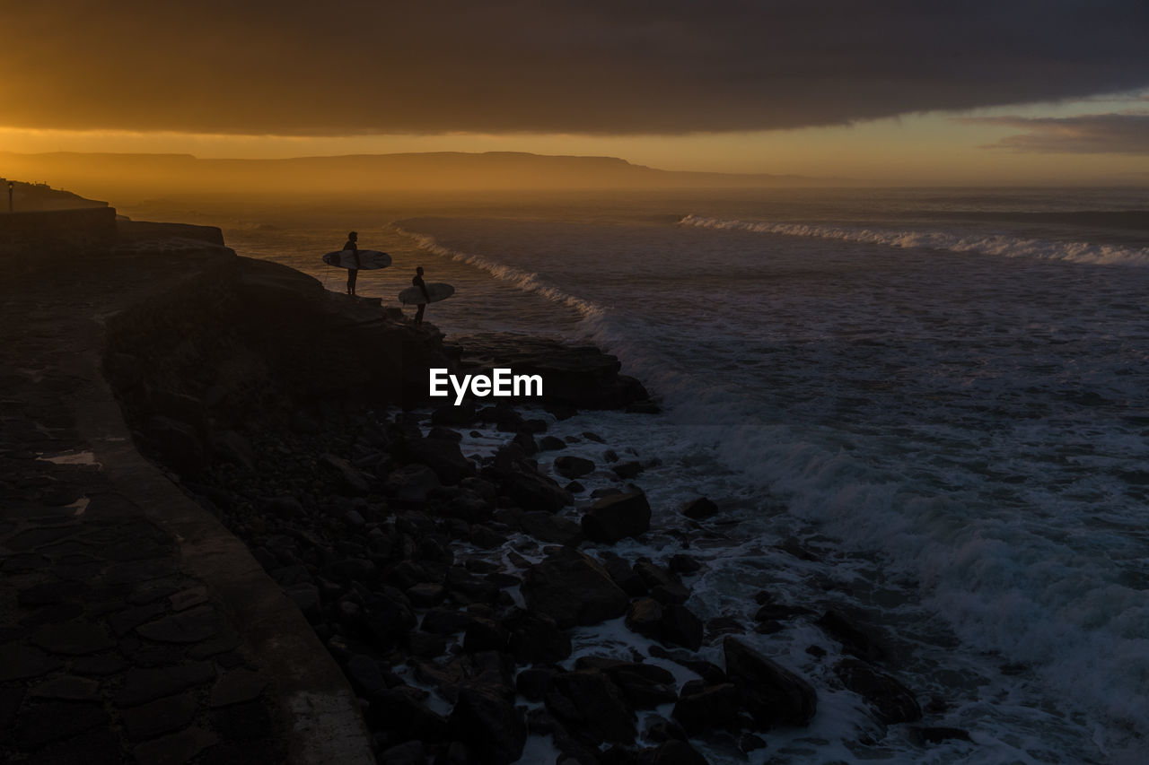 Surfers looking at sea at dusk