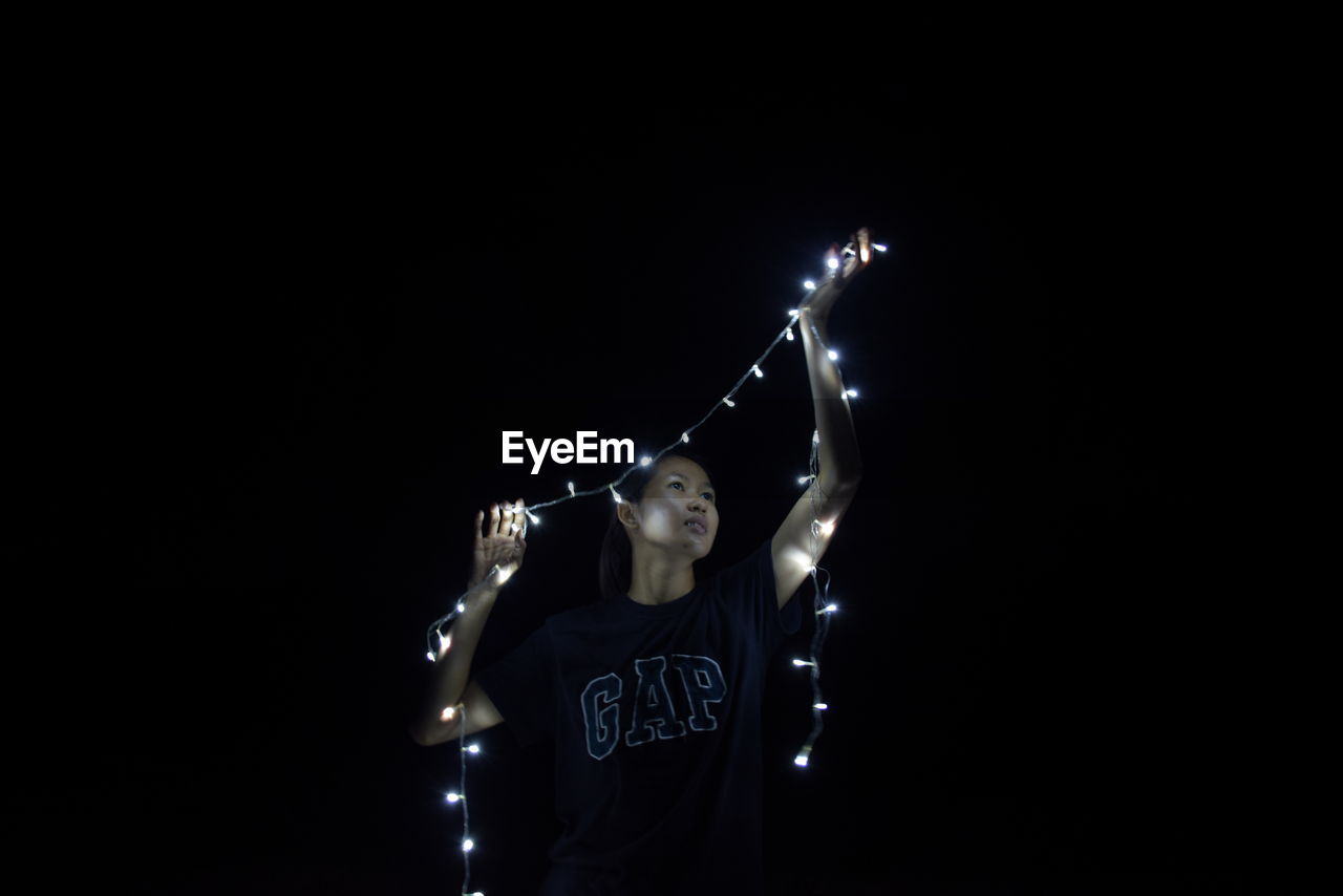 WOMAN STANDING AGAINST ILLUMINATED LIGHTING EQUIPMENT