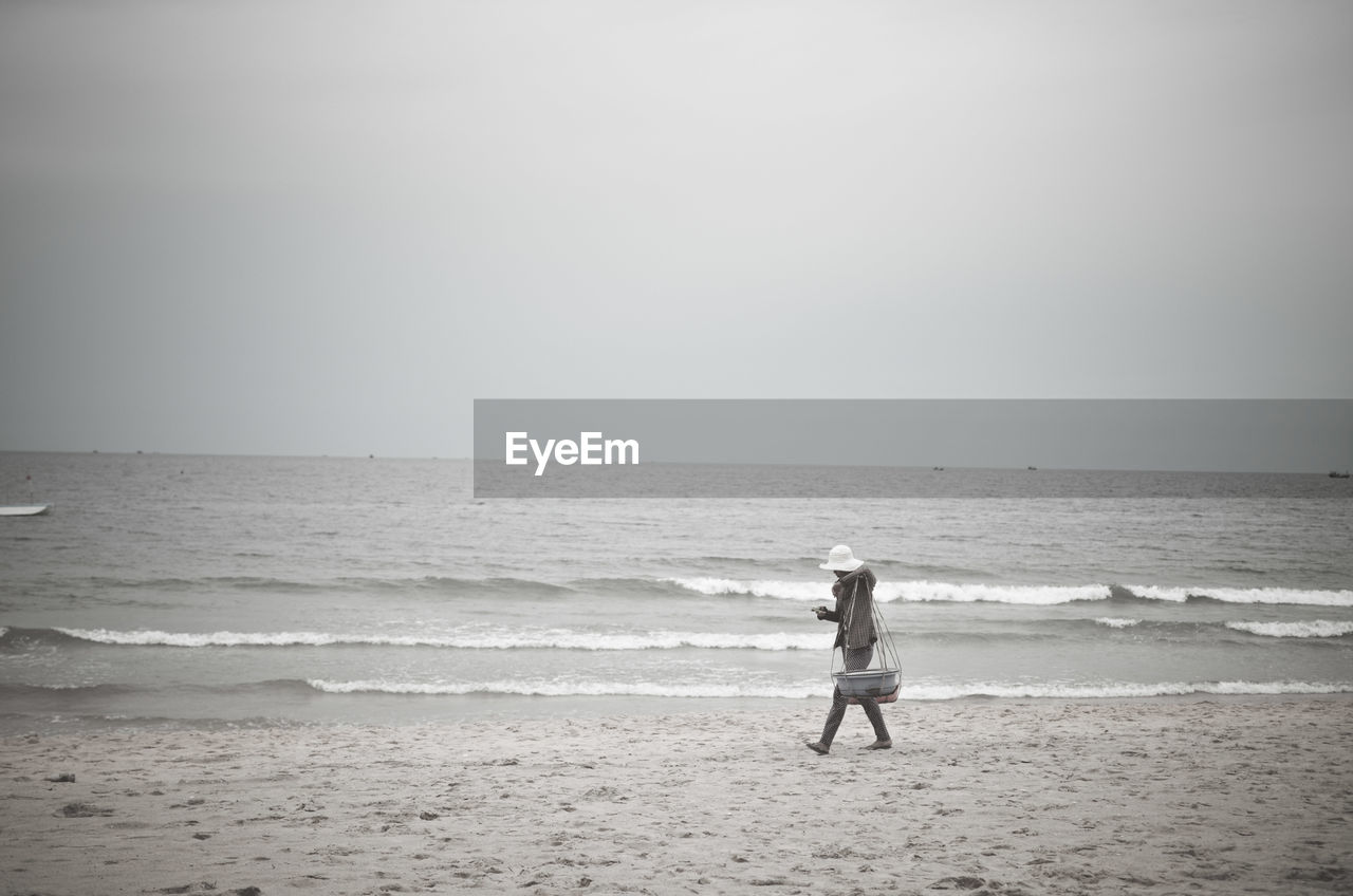 Side view of fisherman walking on beach against clear sky