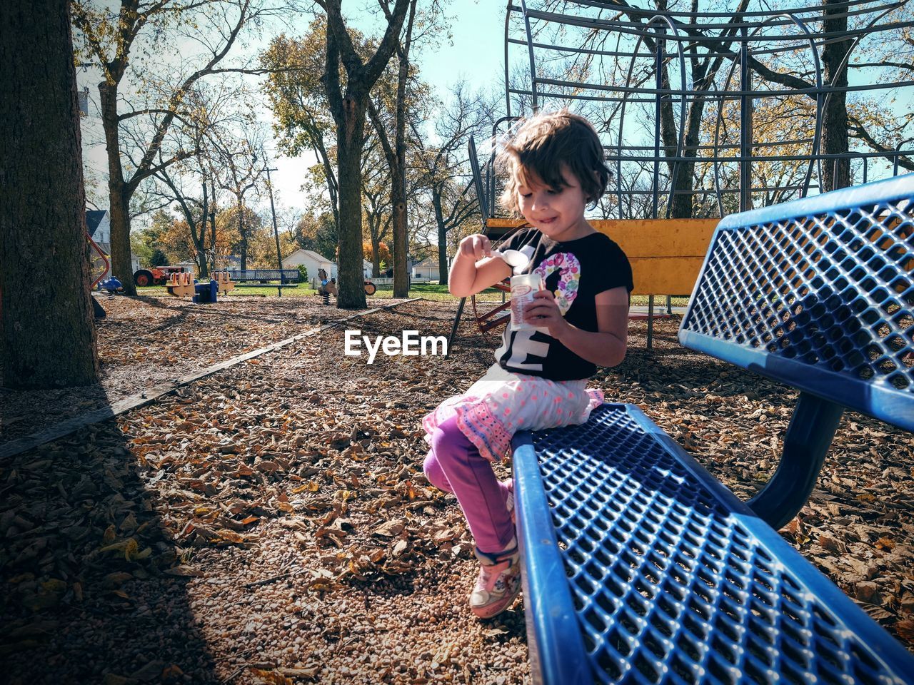 Girl eating food while sitting on bench against trees