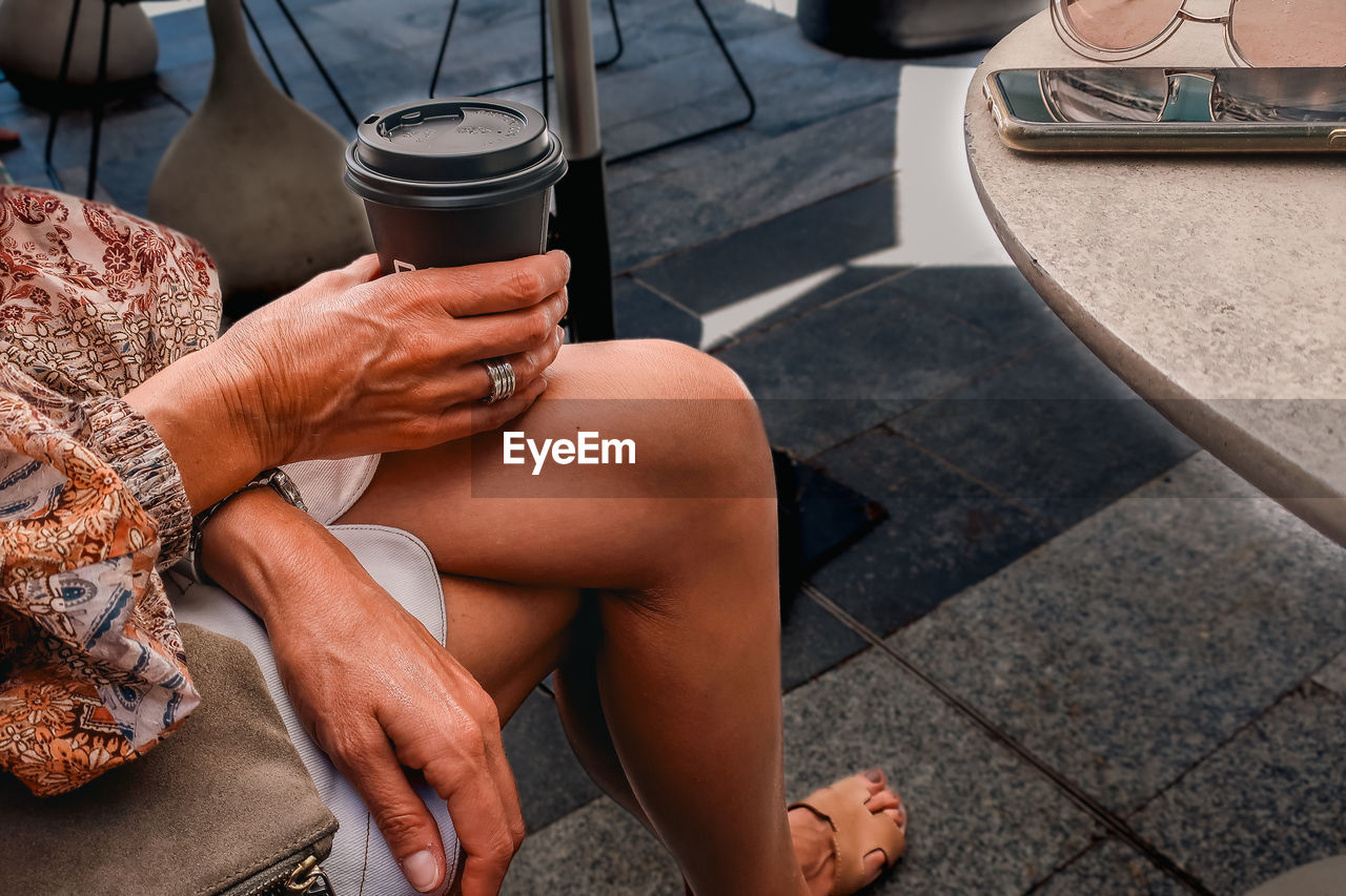Woman sitting crosslegged holding a takeout disposable coffee cup
