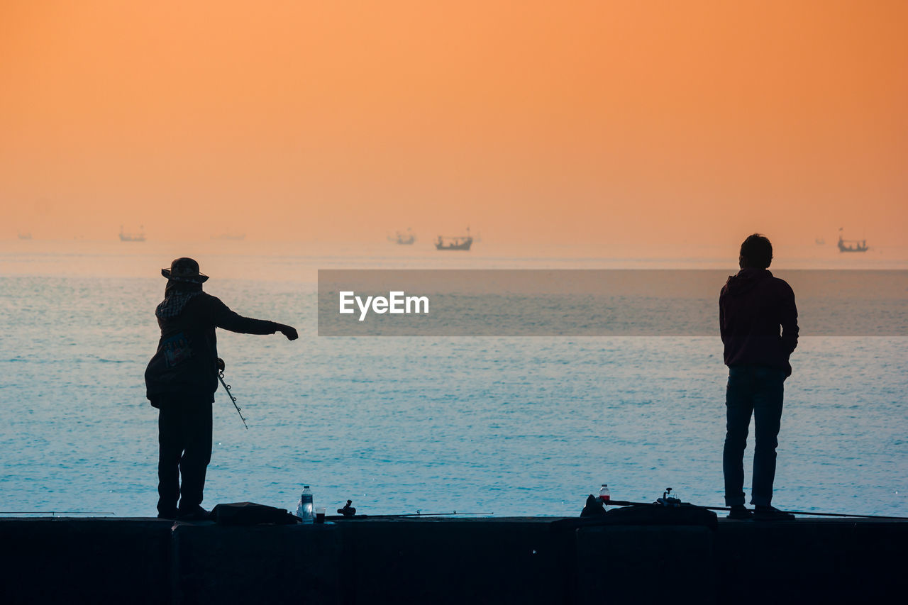 Silhouette men standing on beach against sky during sunset