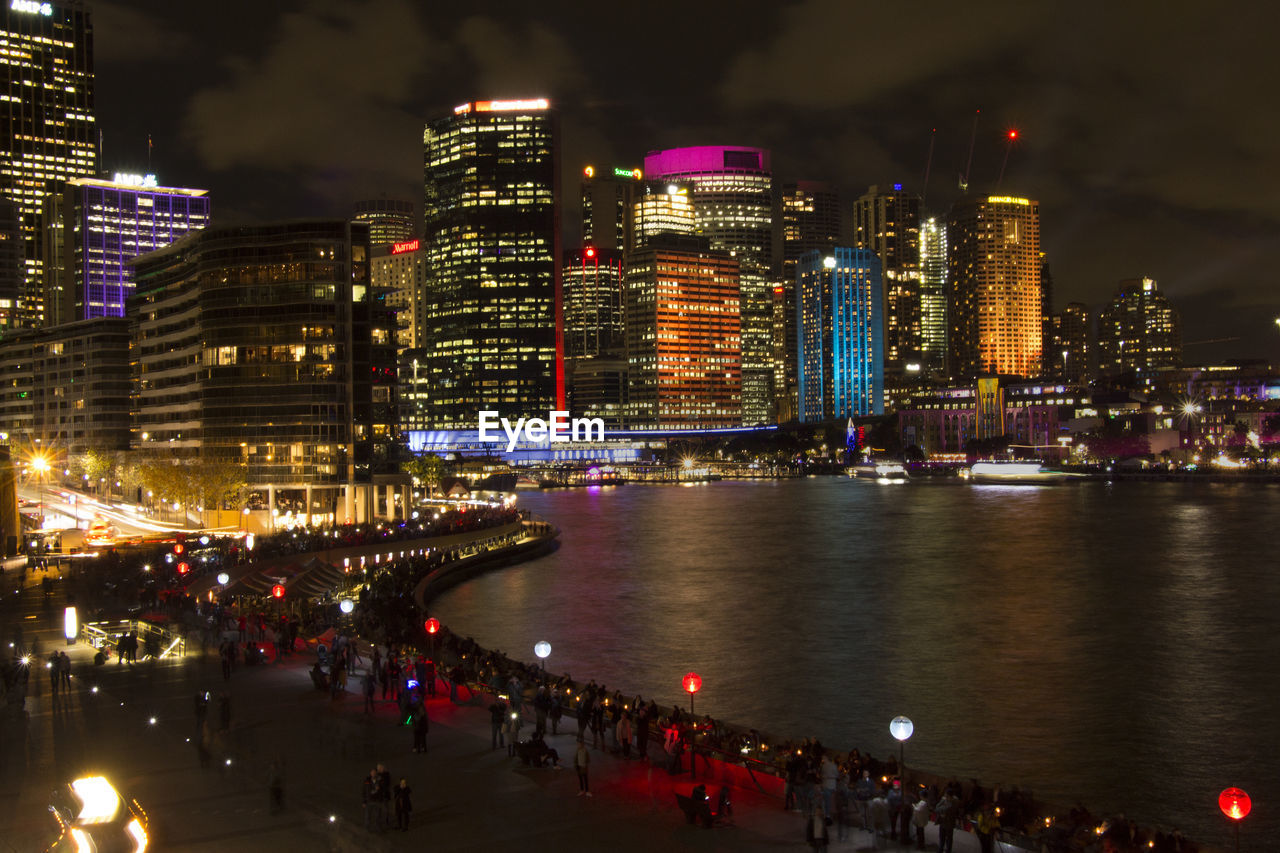 River by illuminated city skyline against sky at night