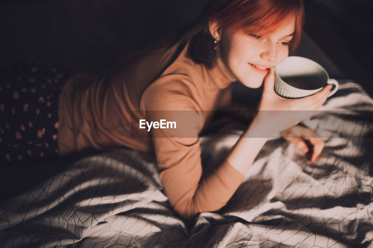 High angle view of girl holding coffee while lying on bed