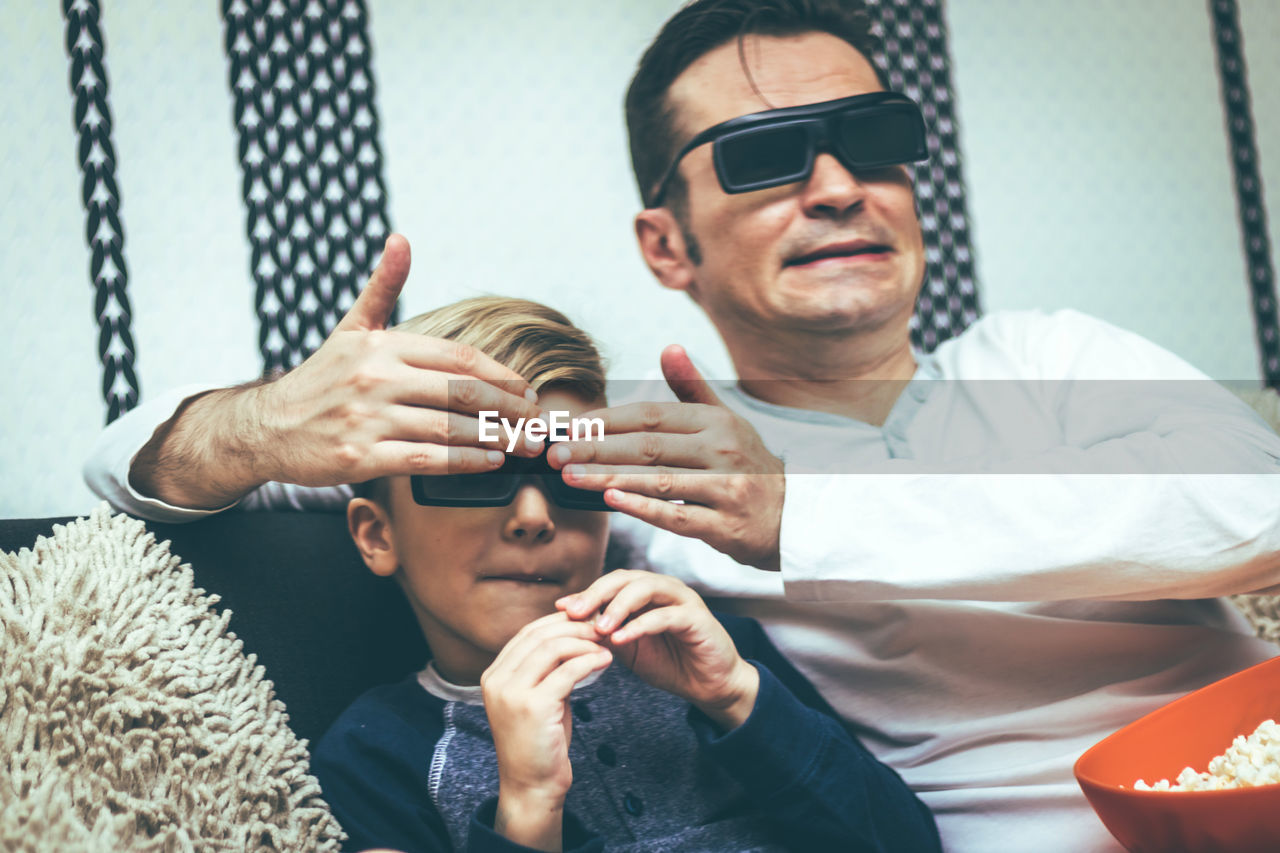 YOUNG MAN WEARING SUNGLASSES WHILE SITTING ON WALL