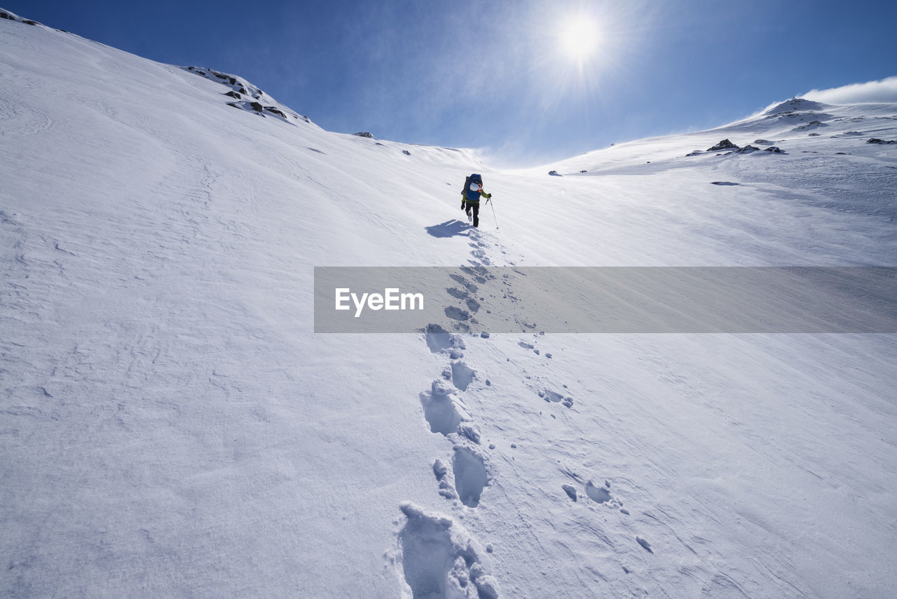 Female hiker aproaching summit of mengensdalstind in deep snow and high wind, moskenesøy, lofoten islands, norway