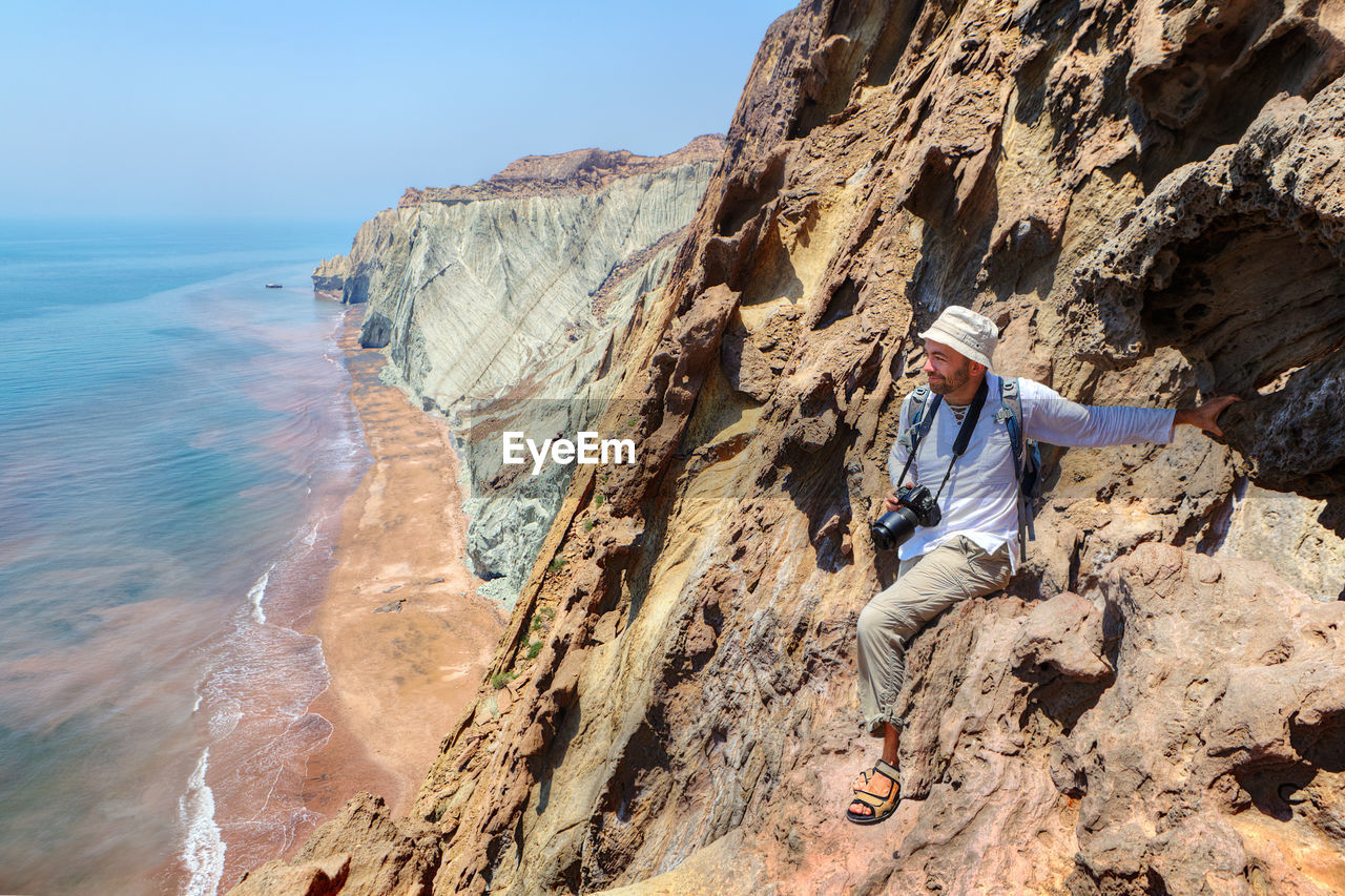 Man with camera on rock formation against sea and sky