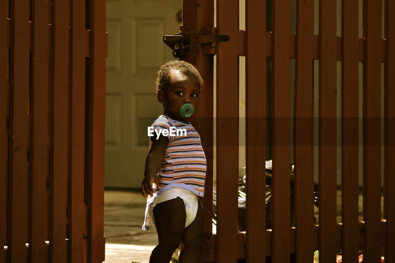 Portrait of boy sucking pacifier by gate