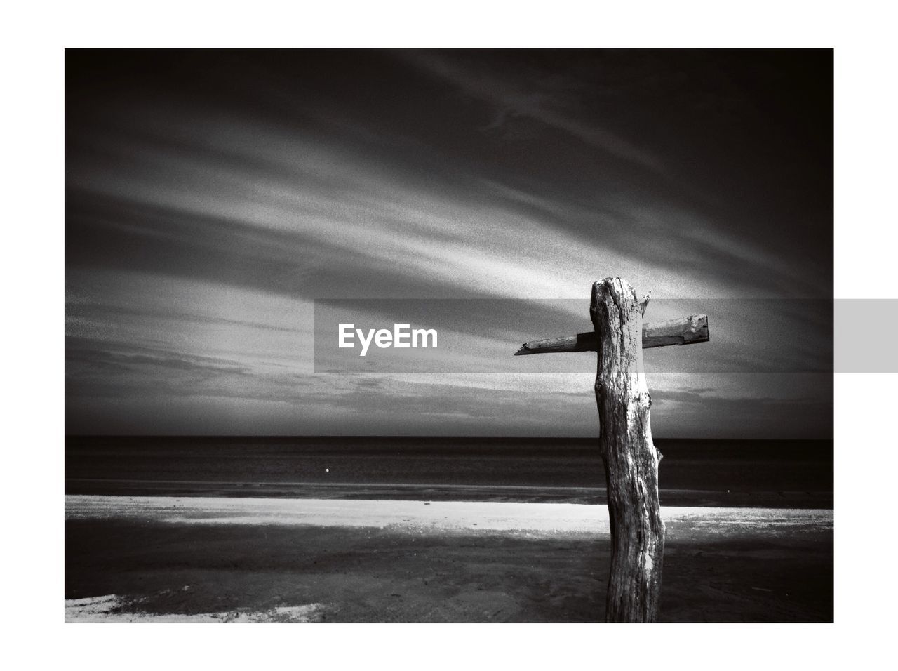 Wooden post on beach against cloudy sky