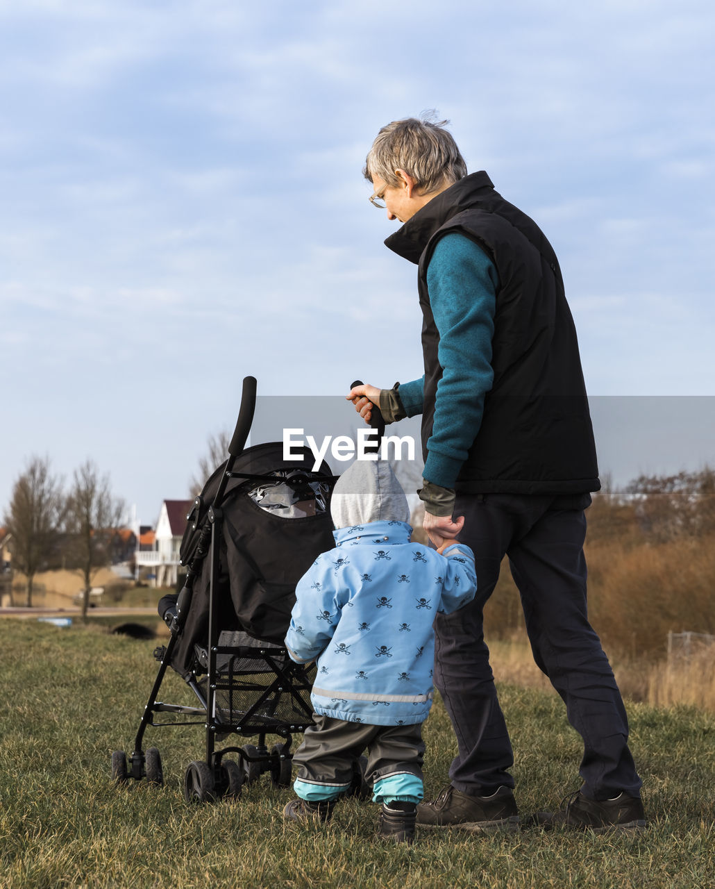 Grandfather and granddaughter walking on field against sky