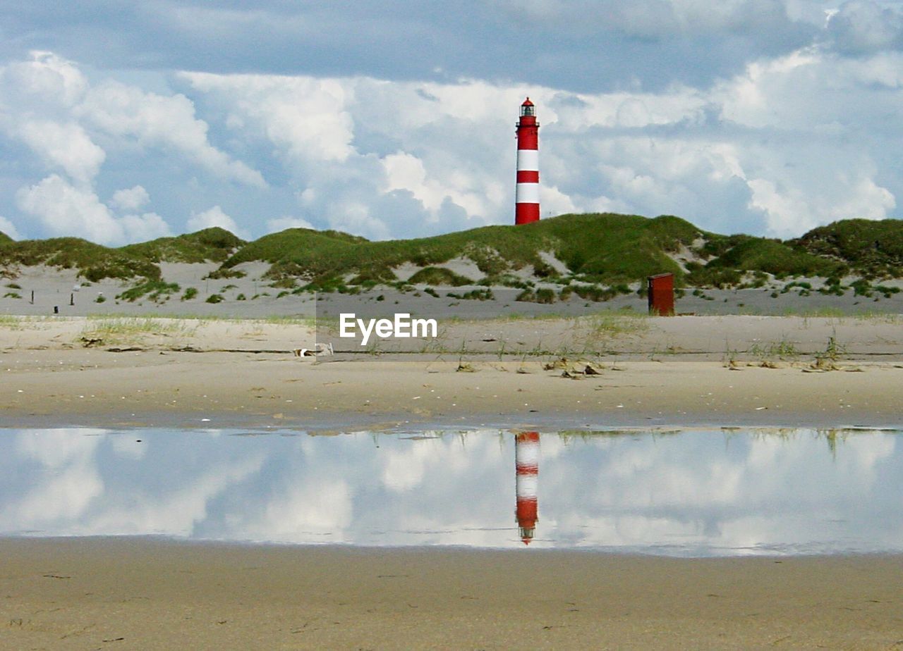 Lighthouse by puddle against sky