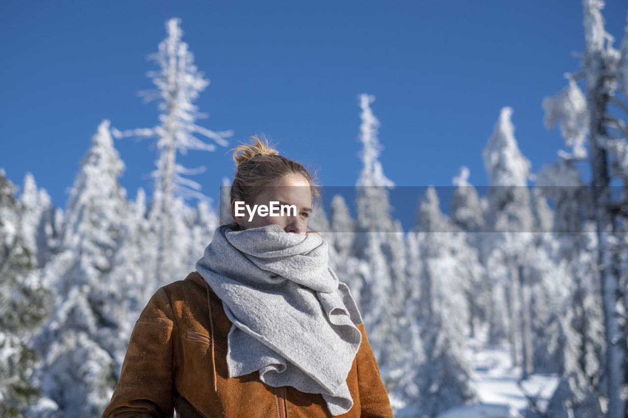 Young woman wearing warm clothing while looking away against trees during winter