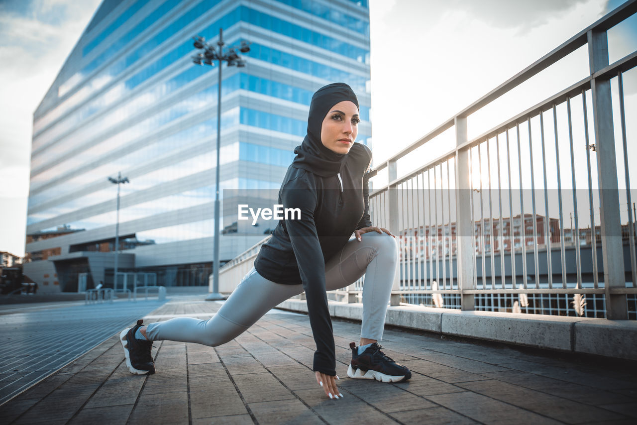 Beautiful woman wearing hijab exercising against building during sunrise