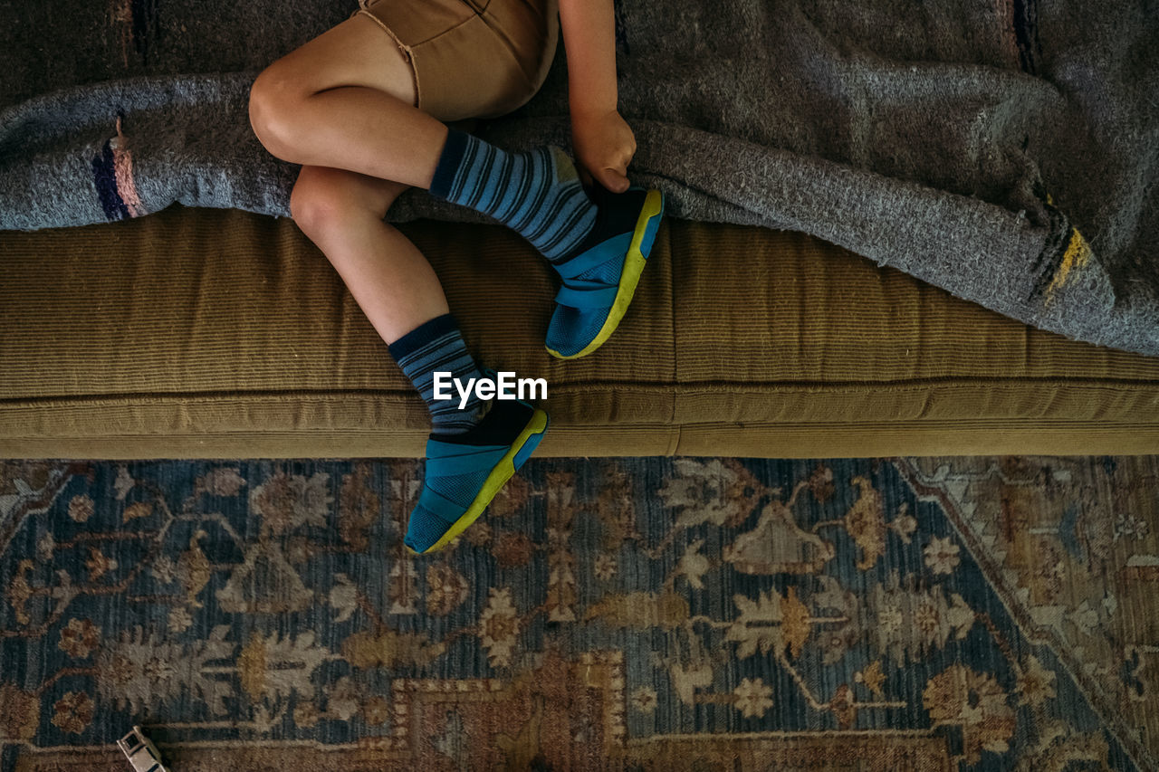 Young boy sitting on couch putting on shoes