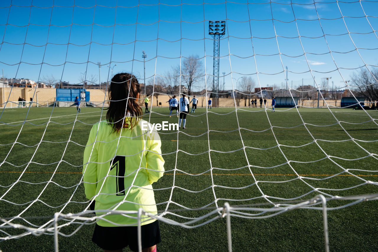 REAR VIEW OF WOMAN PLAYING SOCCER ON FIELD