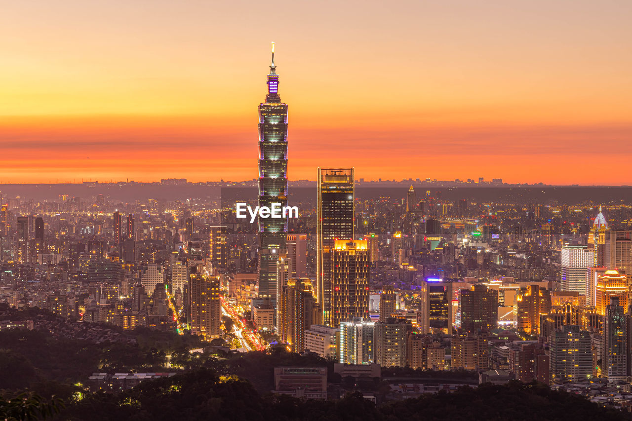 Illuminated buildings in city against sky during sunset