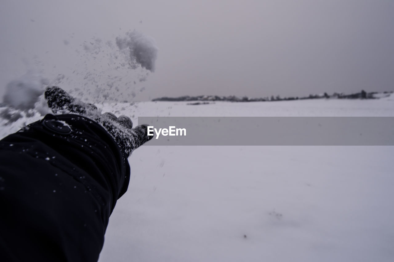 Cropped image of hand over snow covered landscape against sky