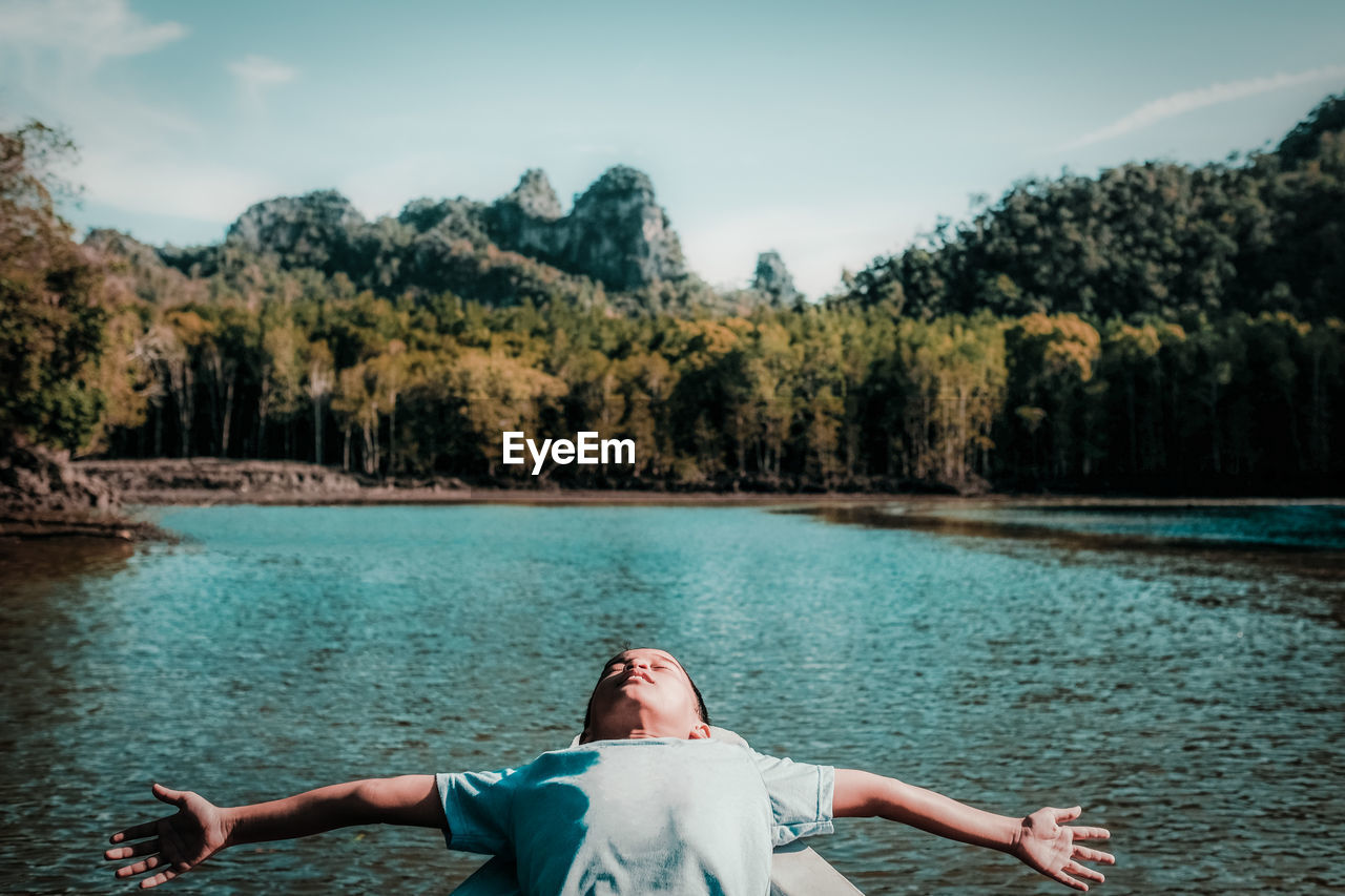Boy lying down at lake against sky