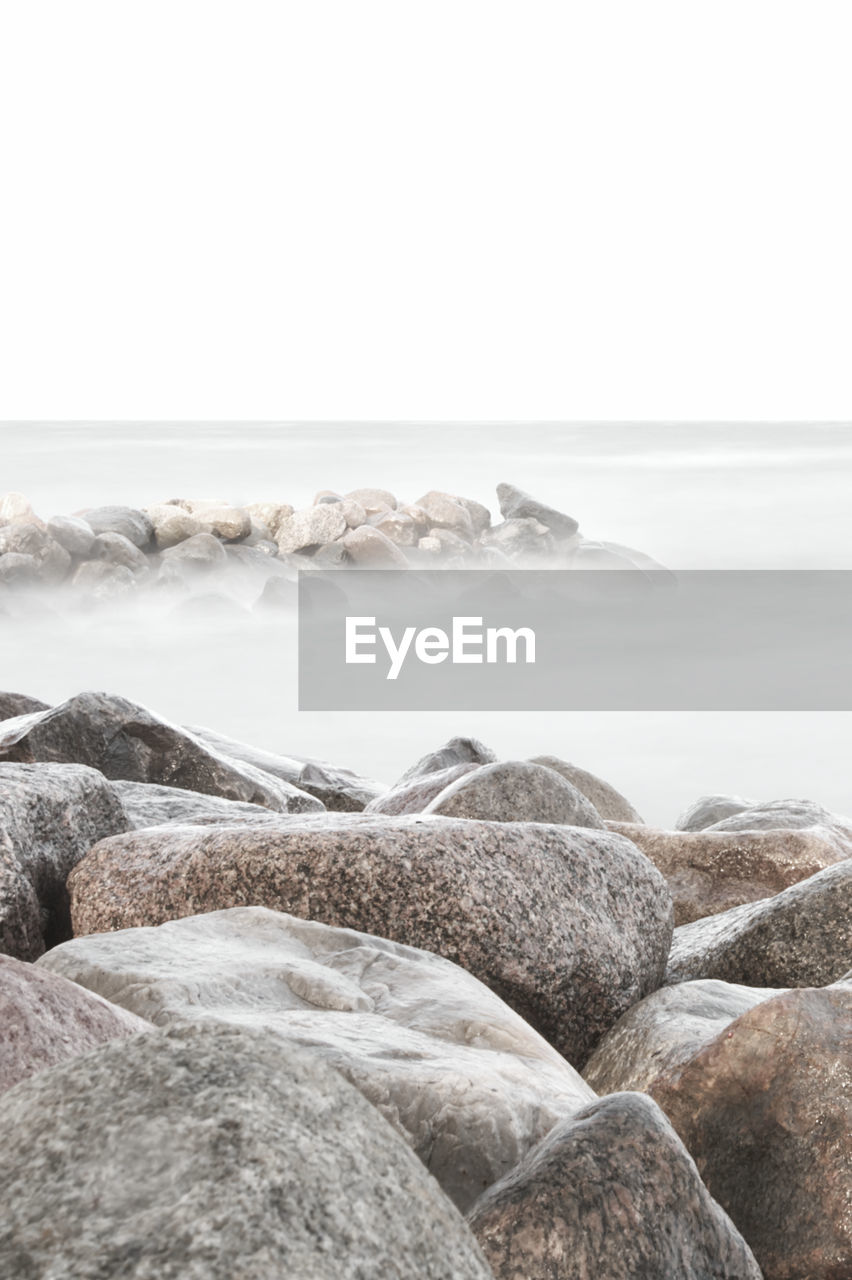 SURFACE LEVEL OF ROCKS ON SHORE AGAINST CLEAR SKY