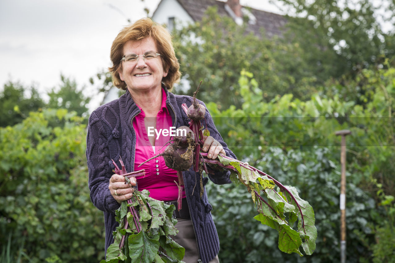 Portrait of smiling woman holding root vegetable against plants