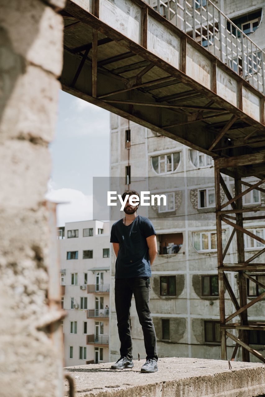 PORTRAIT OF YOUNG MAN STANDING AGAINST BUILDING