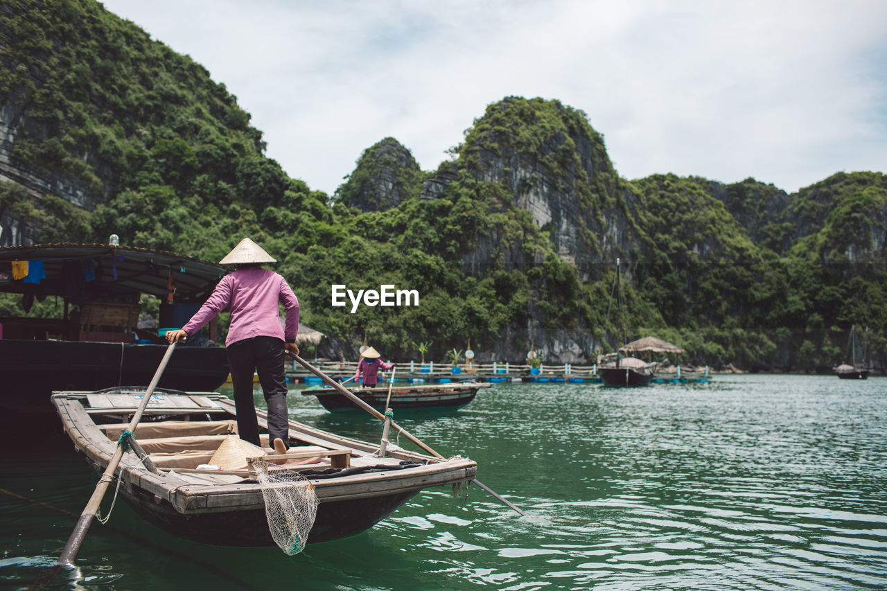 Rear view of woman standing in rowboat on halong bay by mountains