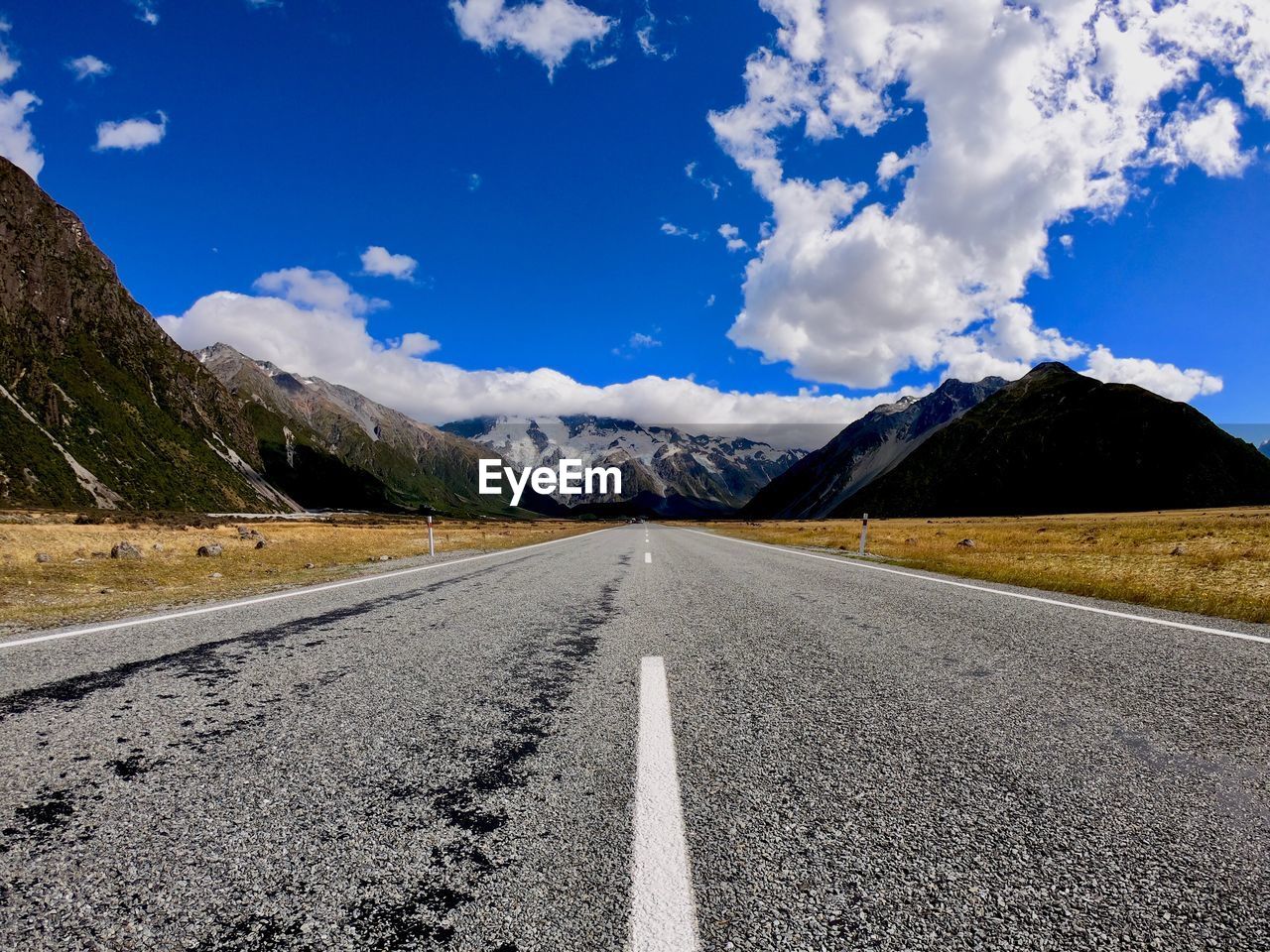 Empty road leading towards mountains against sky