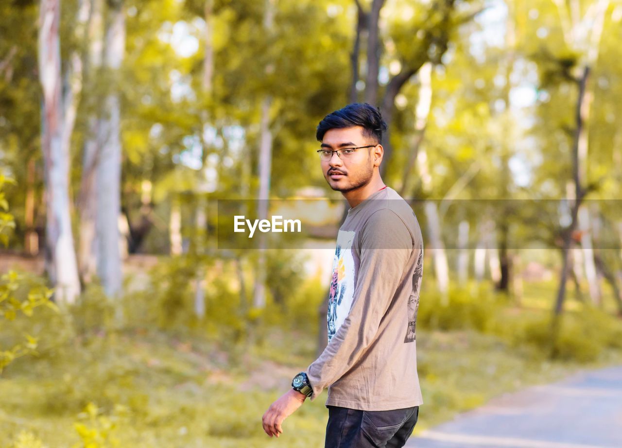 Portrait of young man standing on road against trees