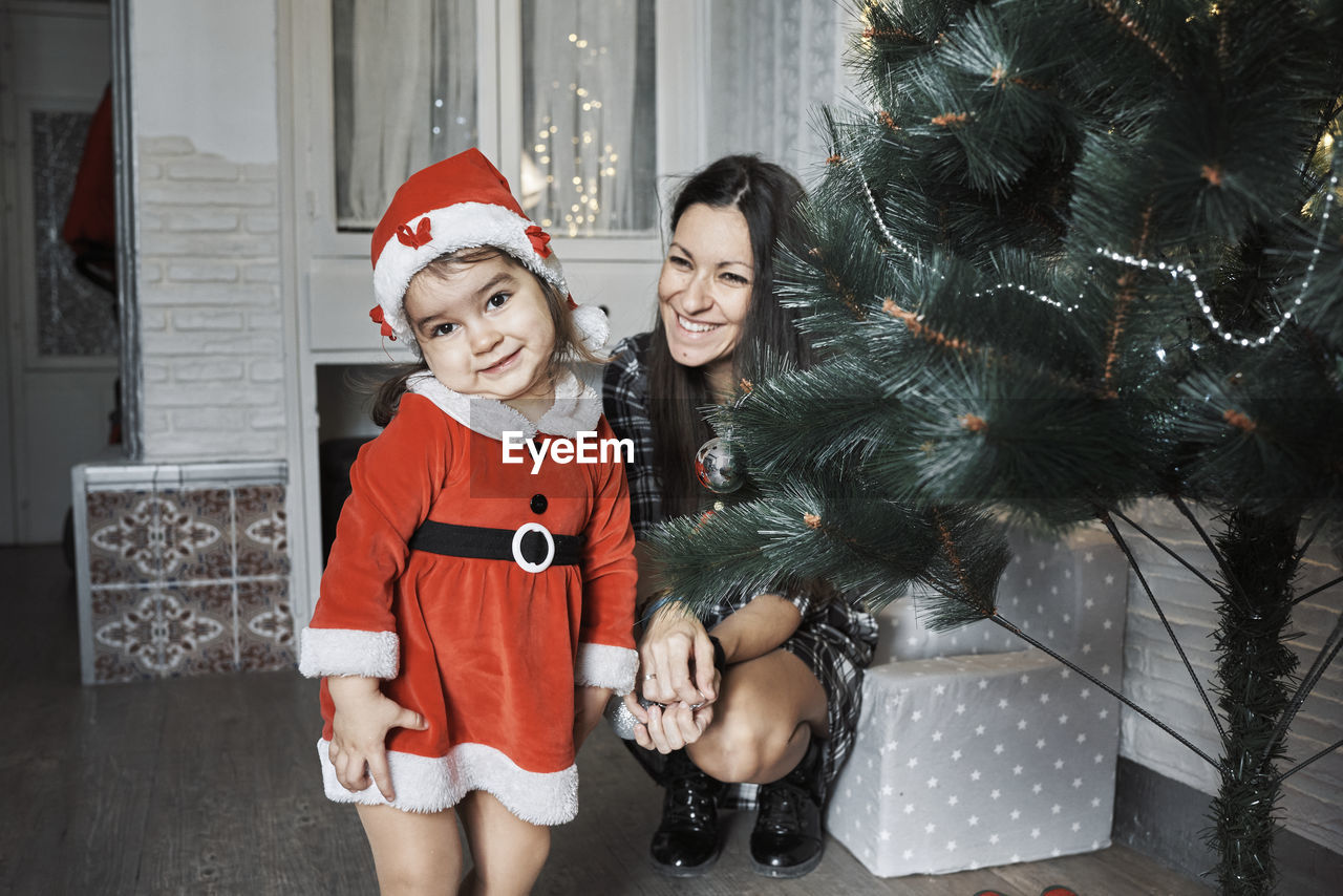 WOMAN STANDING BY CHRISTMAS TREE IN FRONT OF RED AND YELLOW