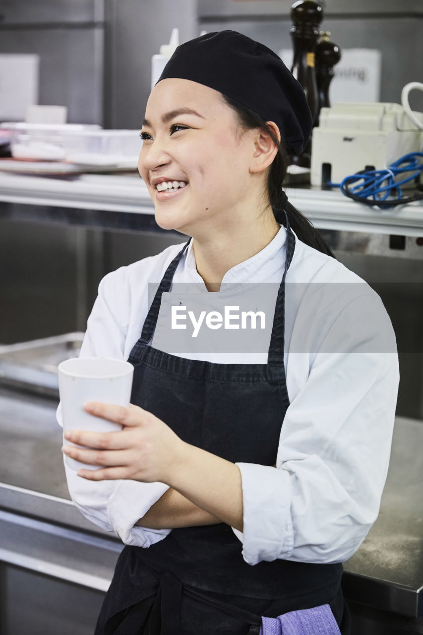 Smiling female chef holding disposable cup in commercial kitchen