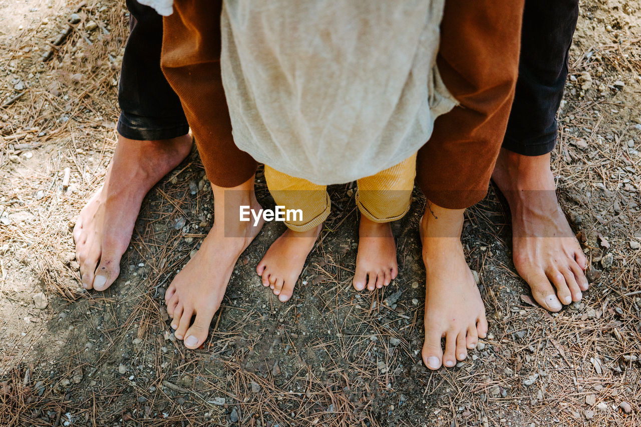 From above of barefoot legs of crop family standing together on ground in forest on sunny day