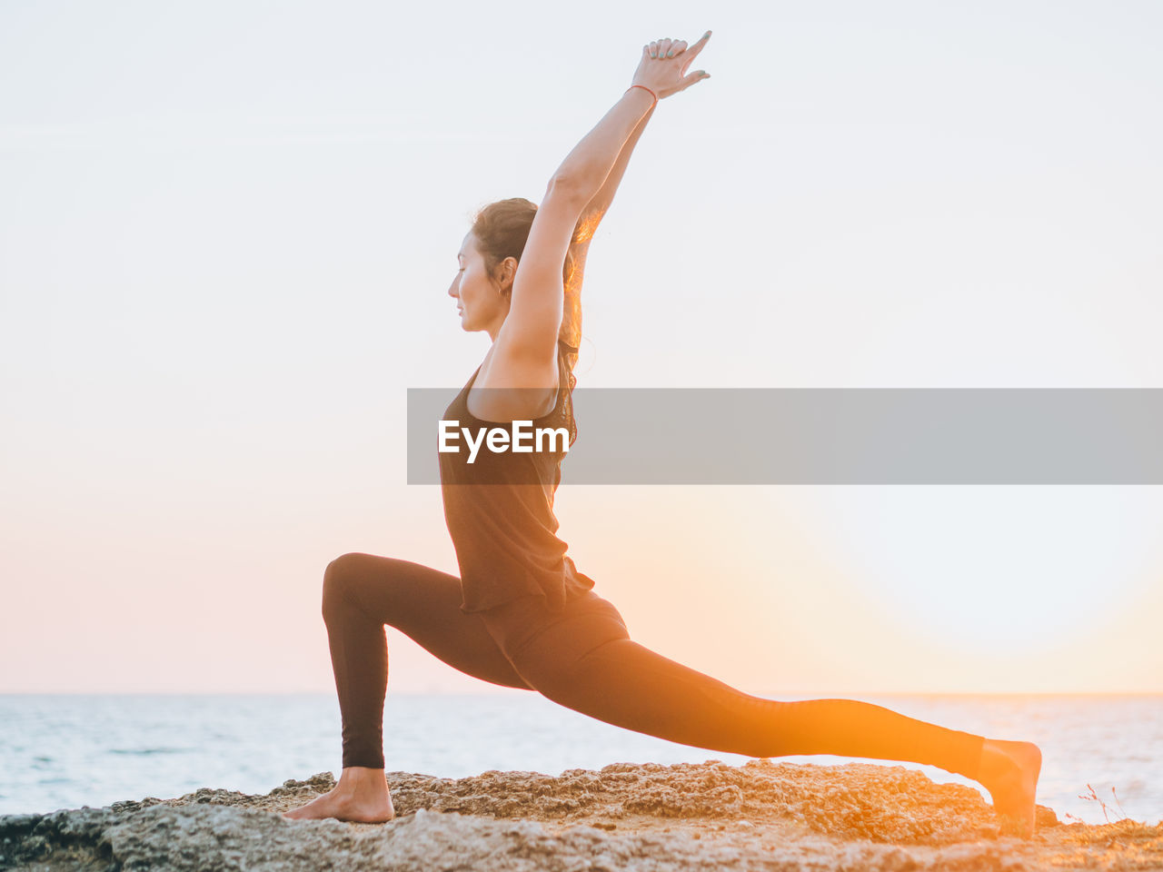 Full length of woman doing yoga at beach against sky during sunset