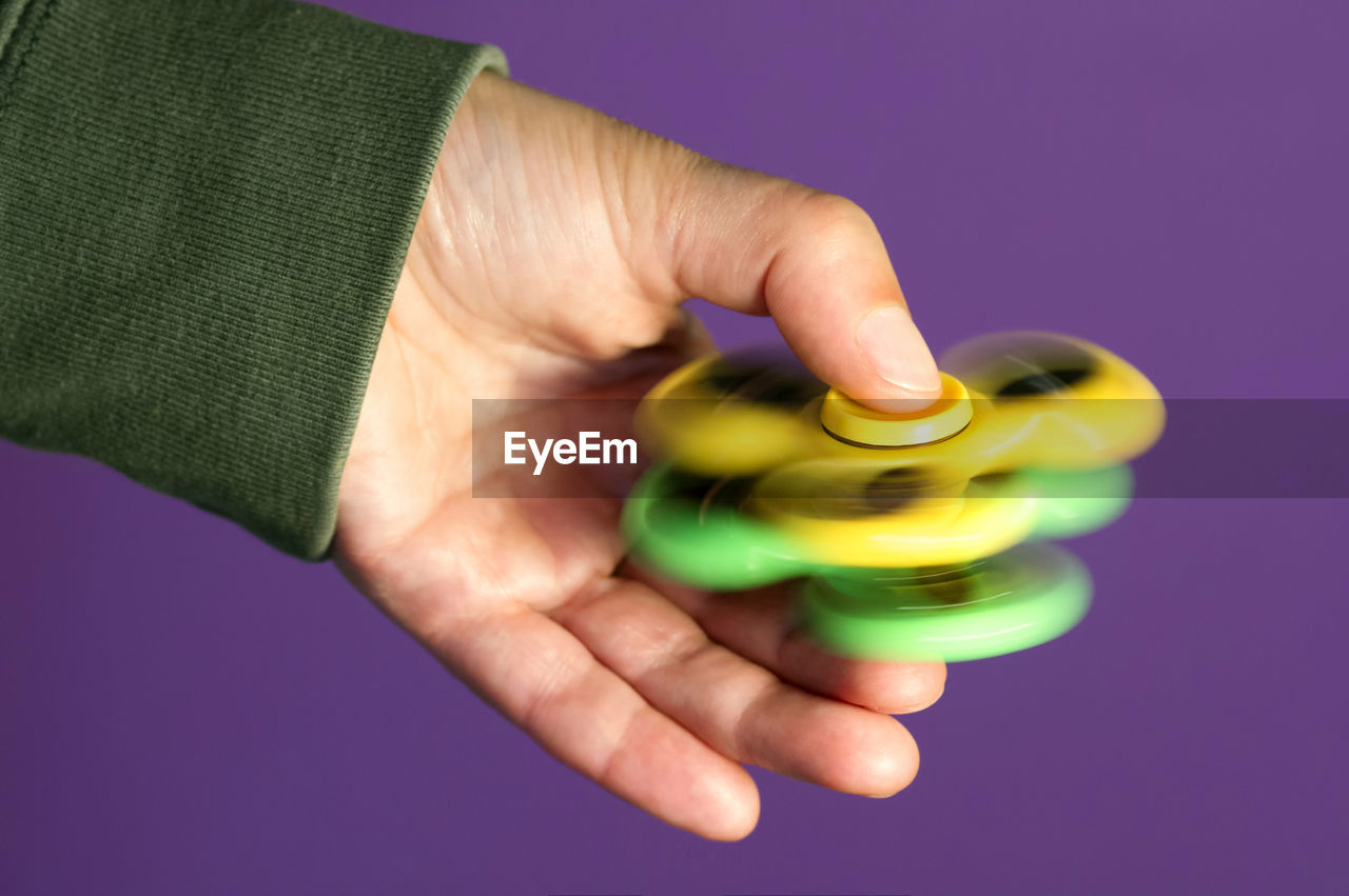 Close-up of cropped hand spinning fidget against purple background