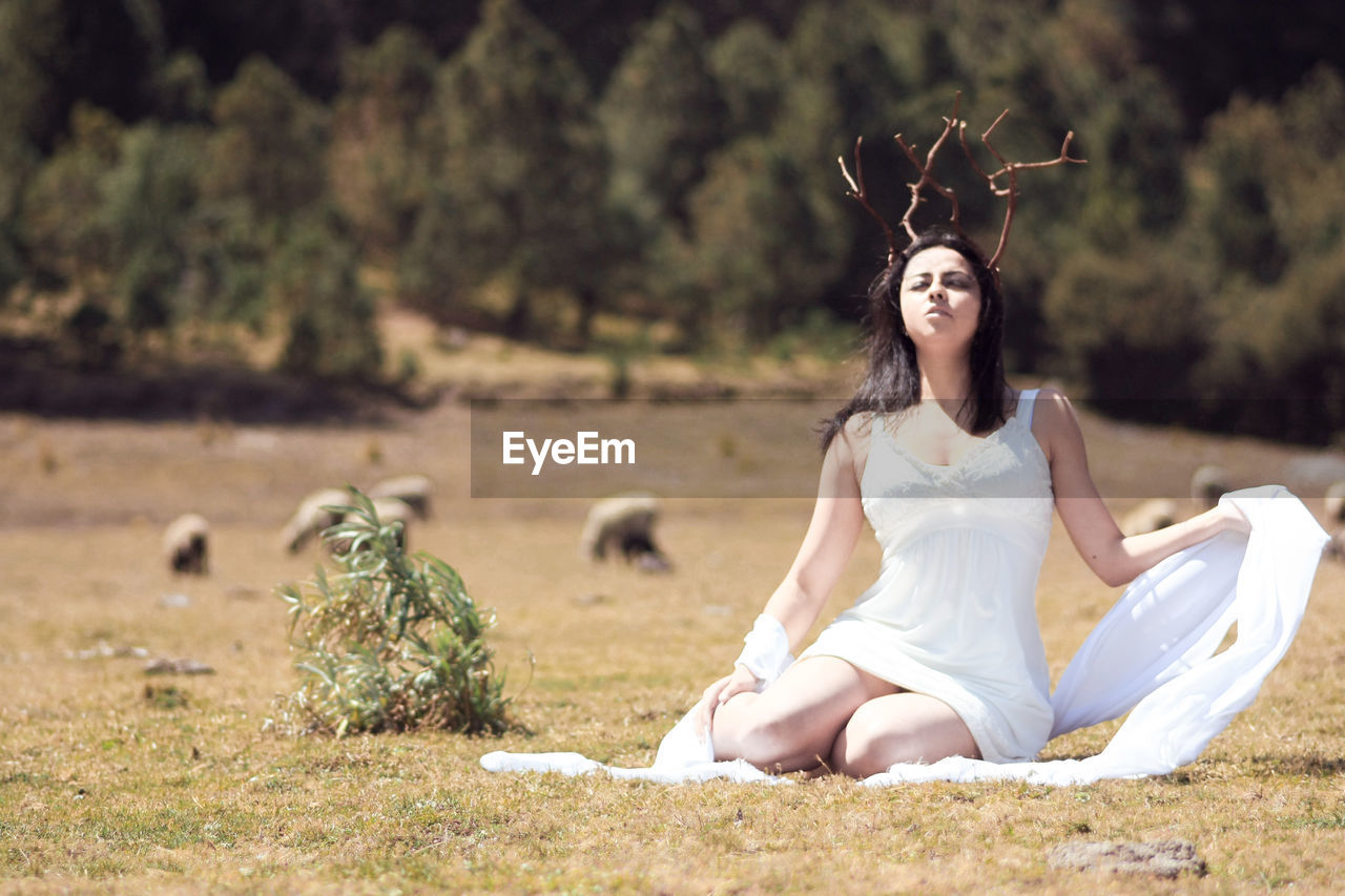 Beautiful woman wearing artificial horn while sitting on field