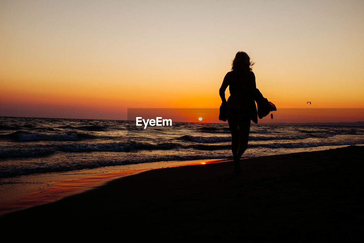 Rear view of silhouette woman walking at beach against clear sky during sunset