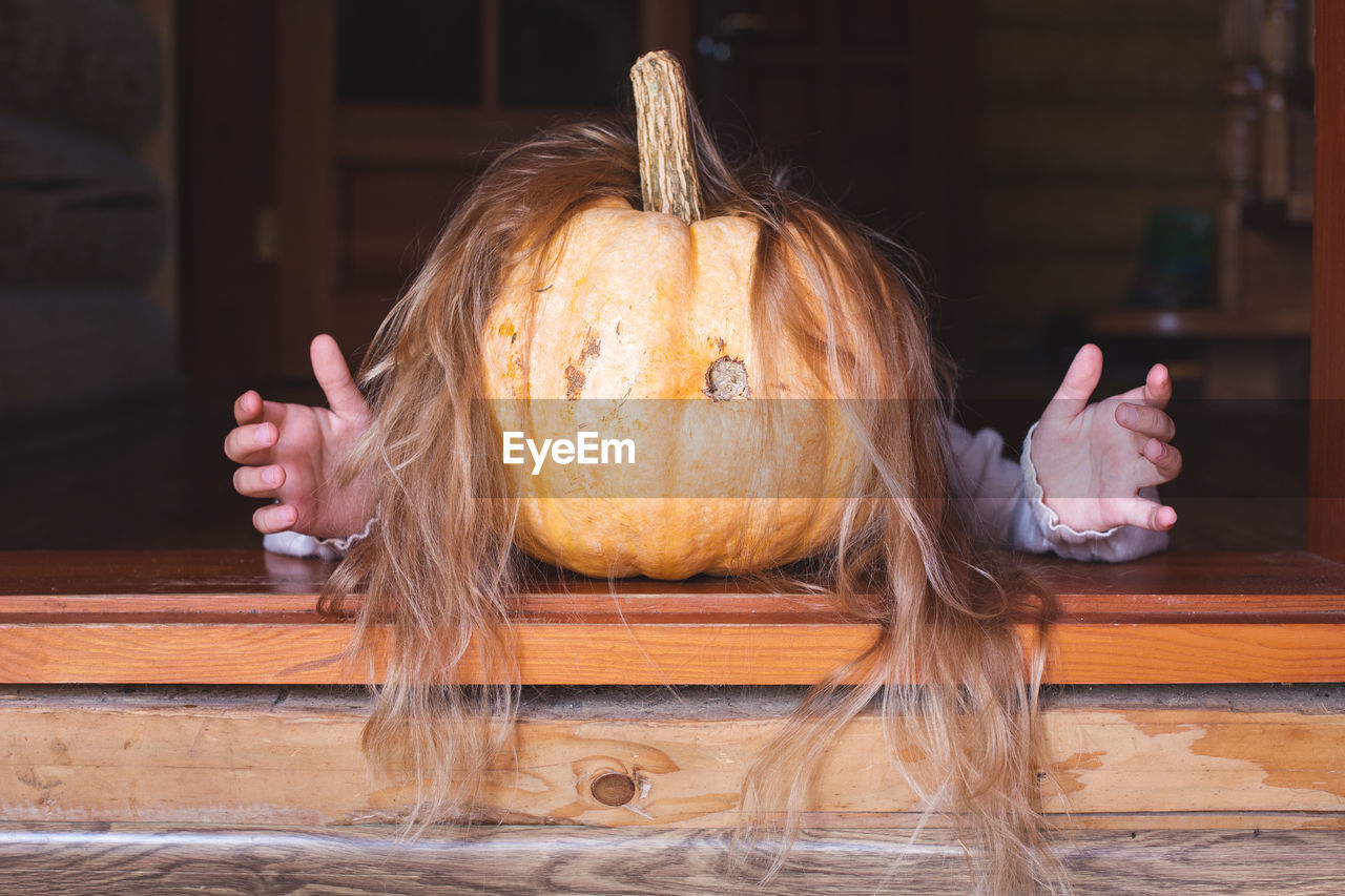 On a threshold lies a orange pumpkin with hair and arms, stretching out his arms forward. halloween
