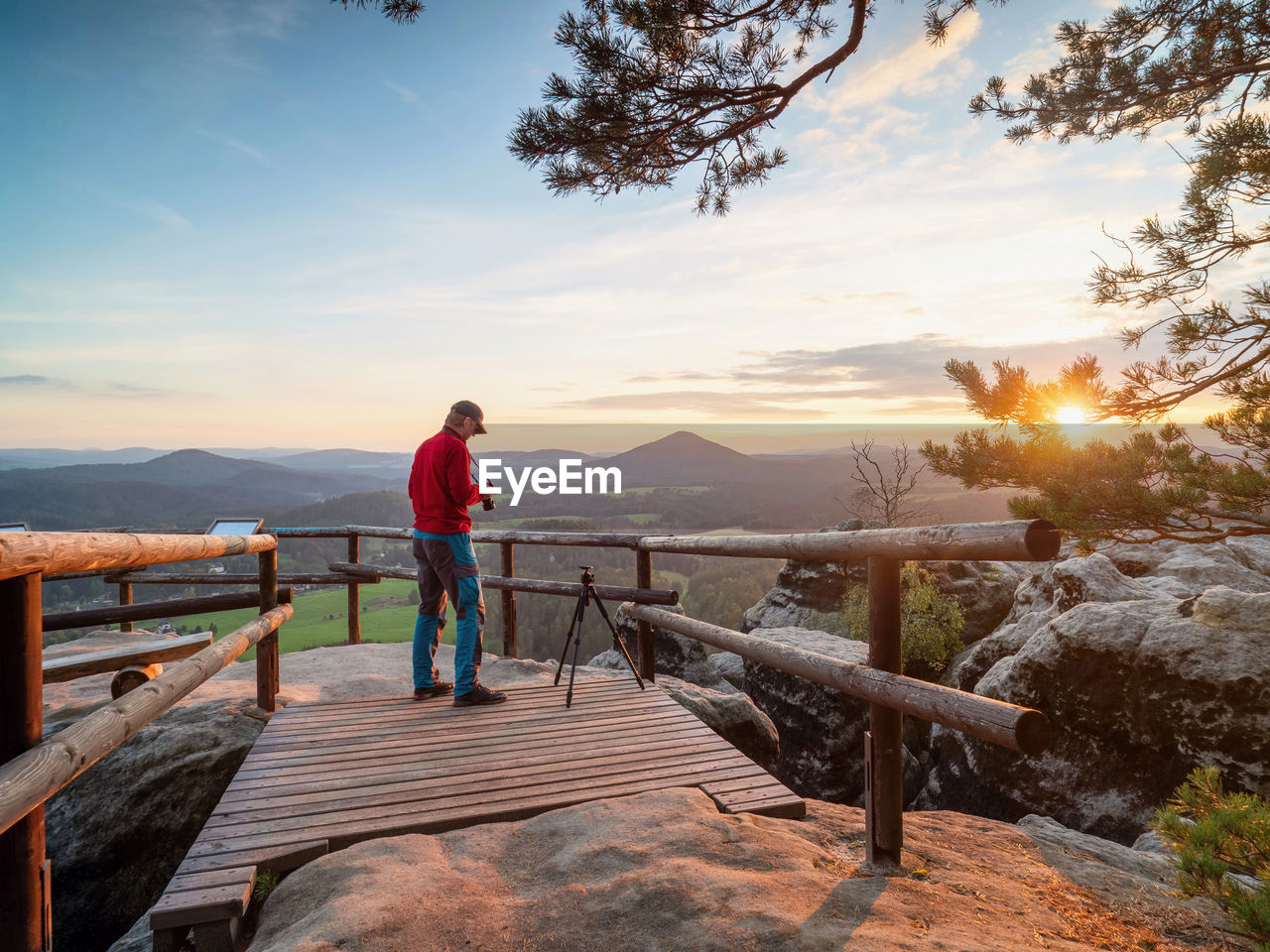 Photographer on tourist view platform takes pictures with big dslr camera in hands. tripod empty