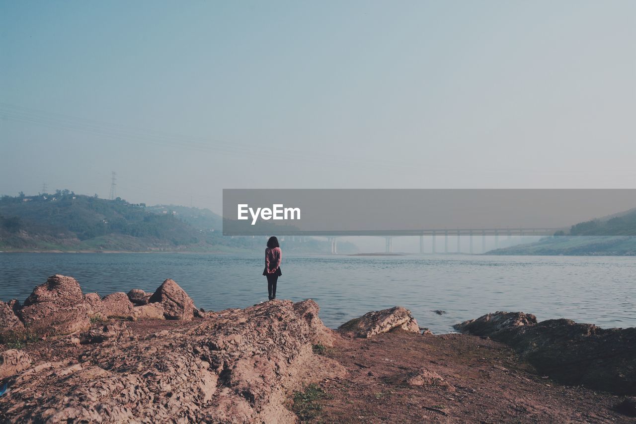 Rear view of woman standing on rock formation by sea against sky