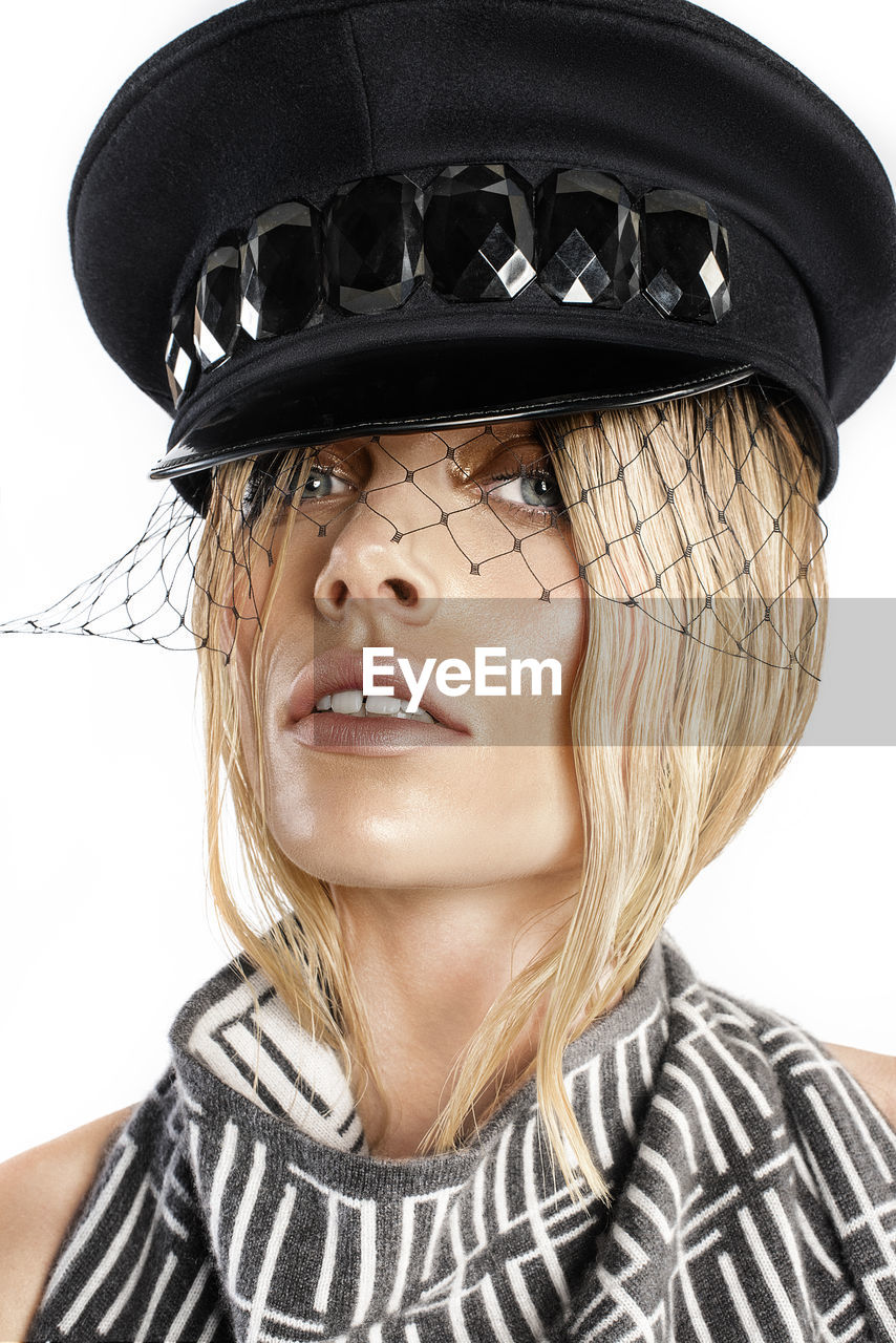 Close-up portrait of beautiful woman wearing hat against white background